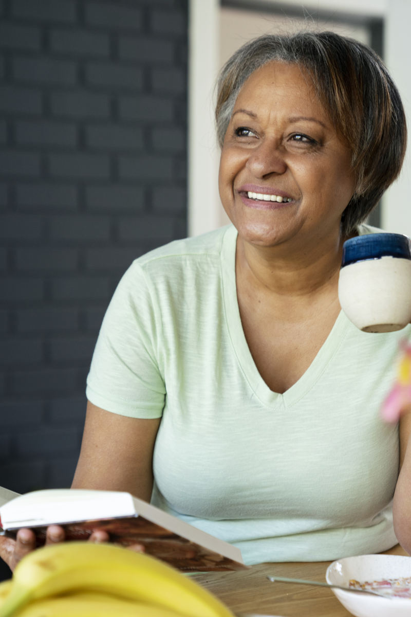 Mulher sorrindo enquanto bebe café e segura um livro